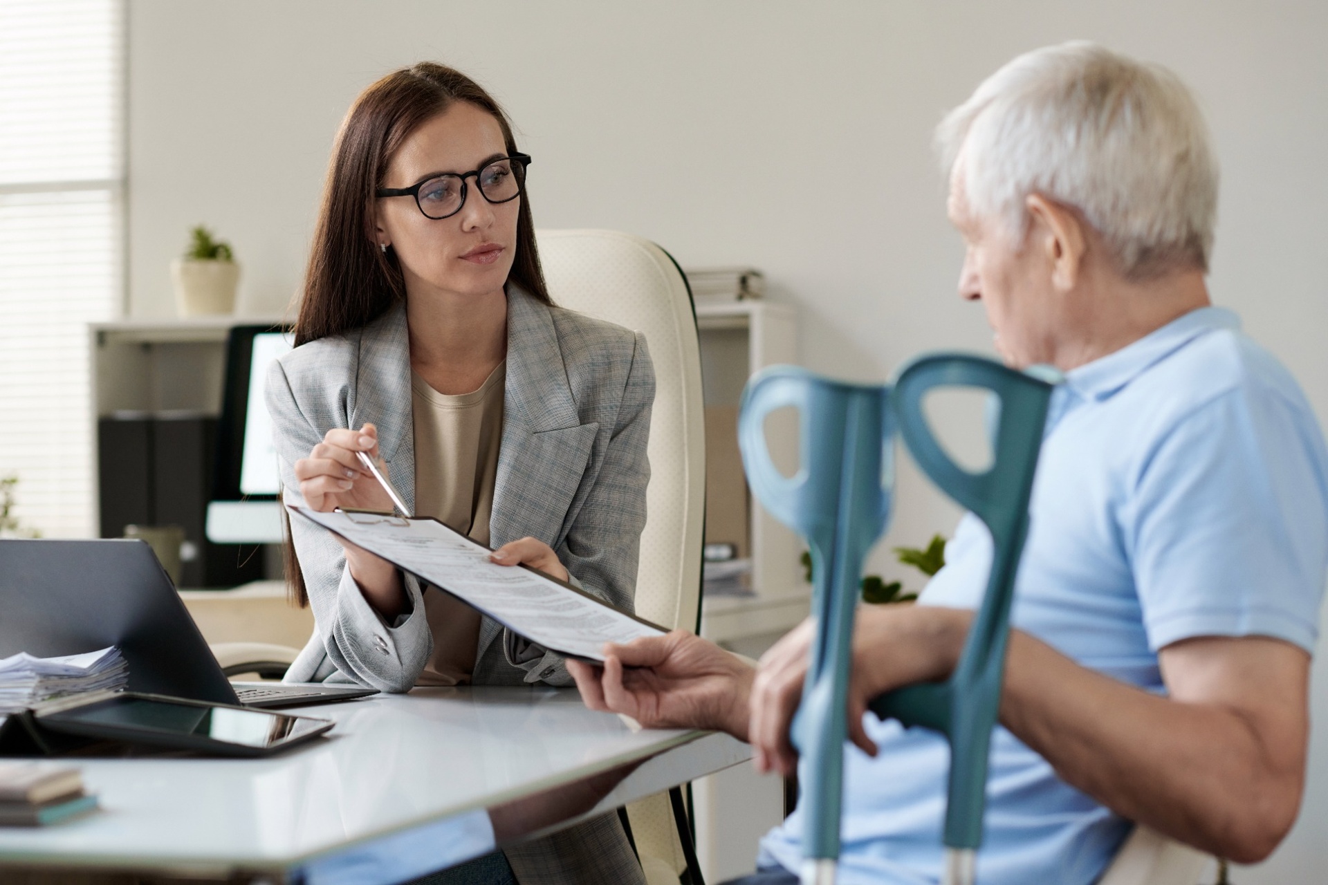 Businesswoman discussing document with senior man using crutches
