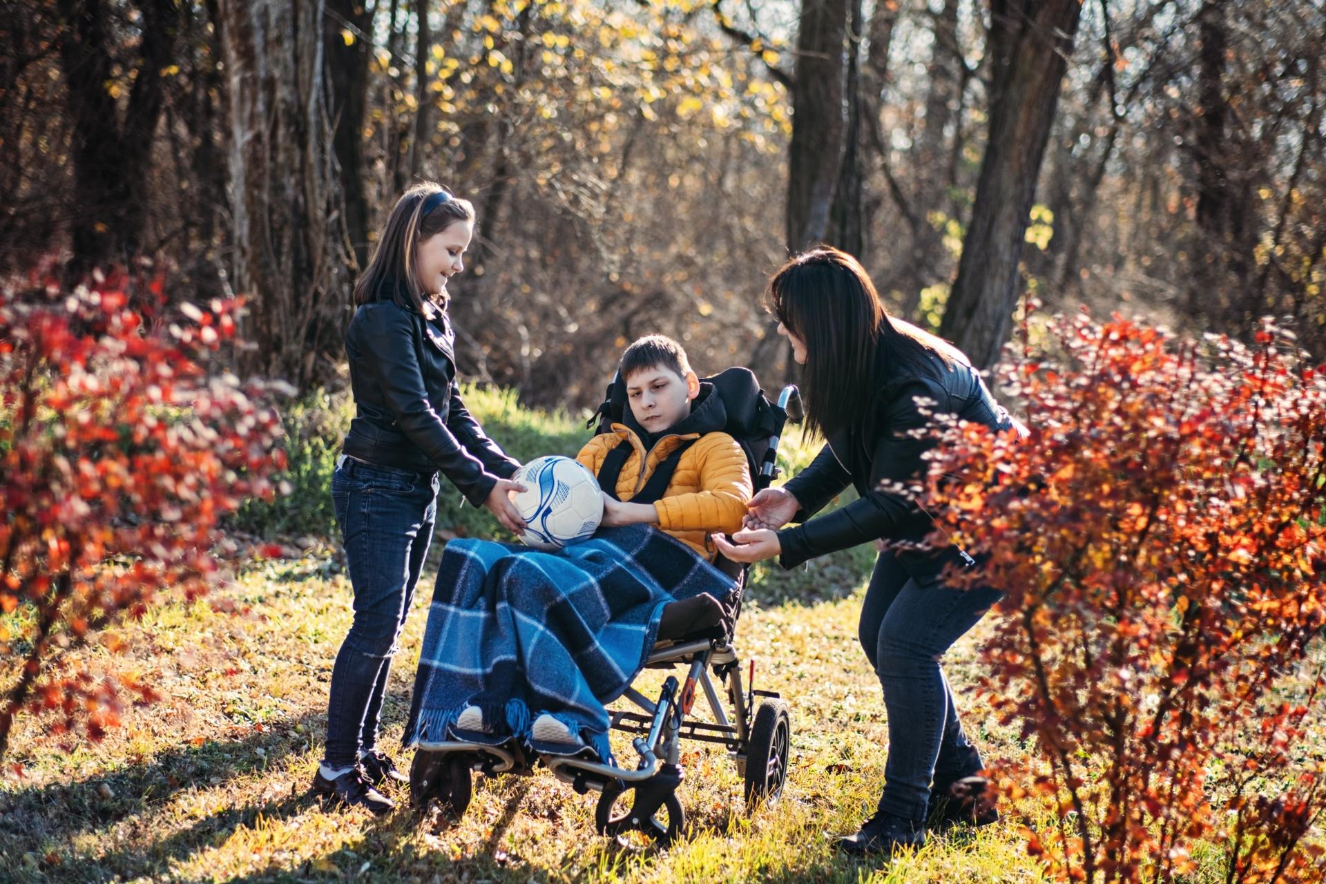 Mother and sibling playing with child in wheelchair in park
