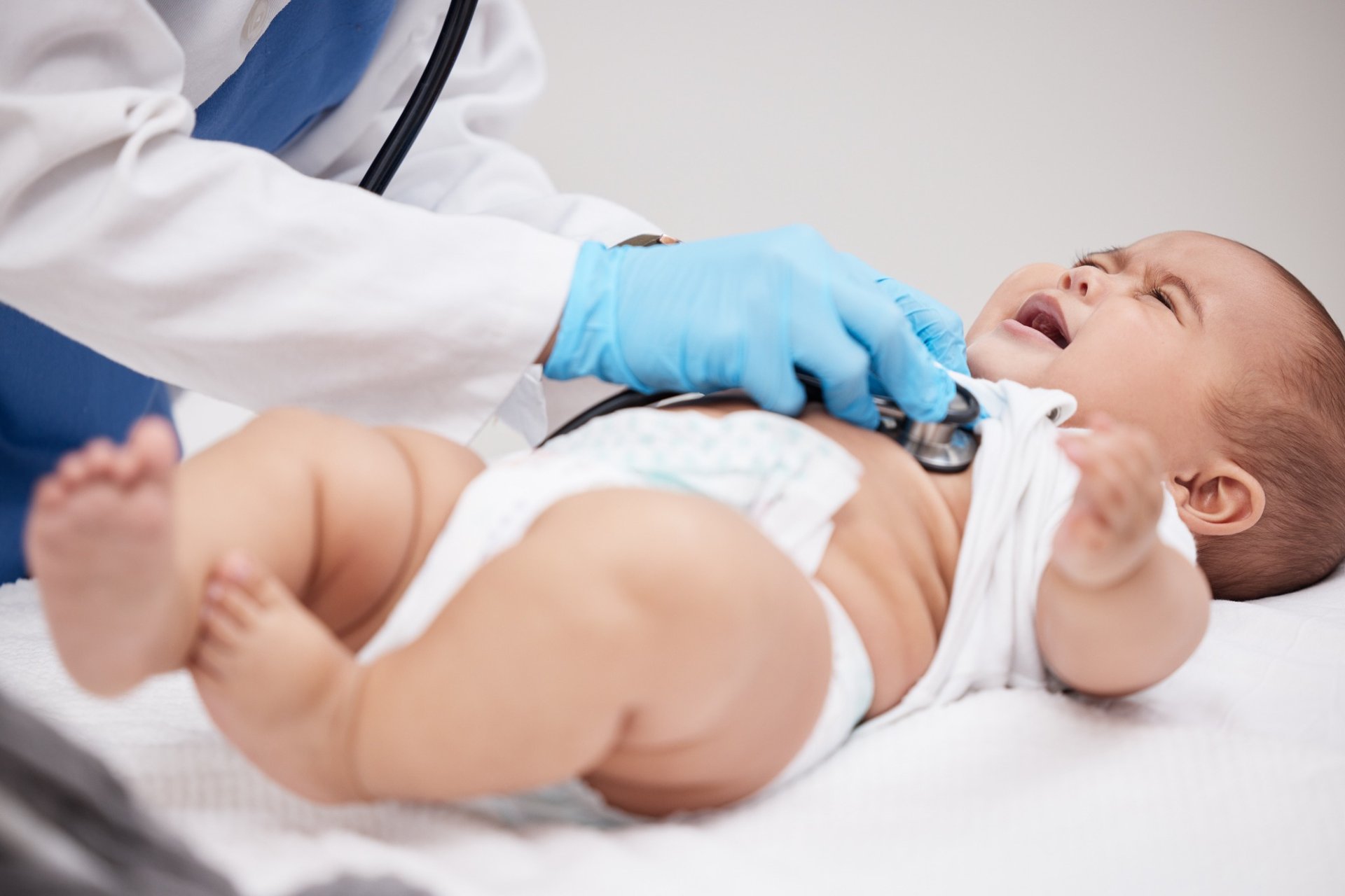 Crying baby being examined by pediatrician with stethoscope