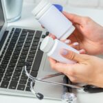 Doctor comparing two white medicine bottles near laptop and stethoscope