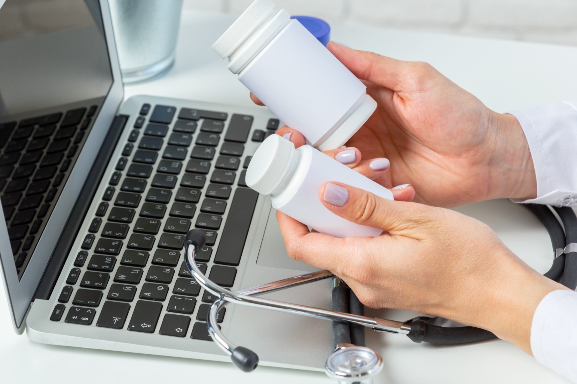 Doctor comparing two white medicine bottles near laptop and stethoscope