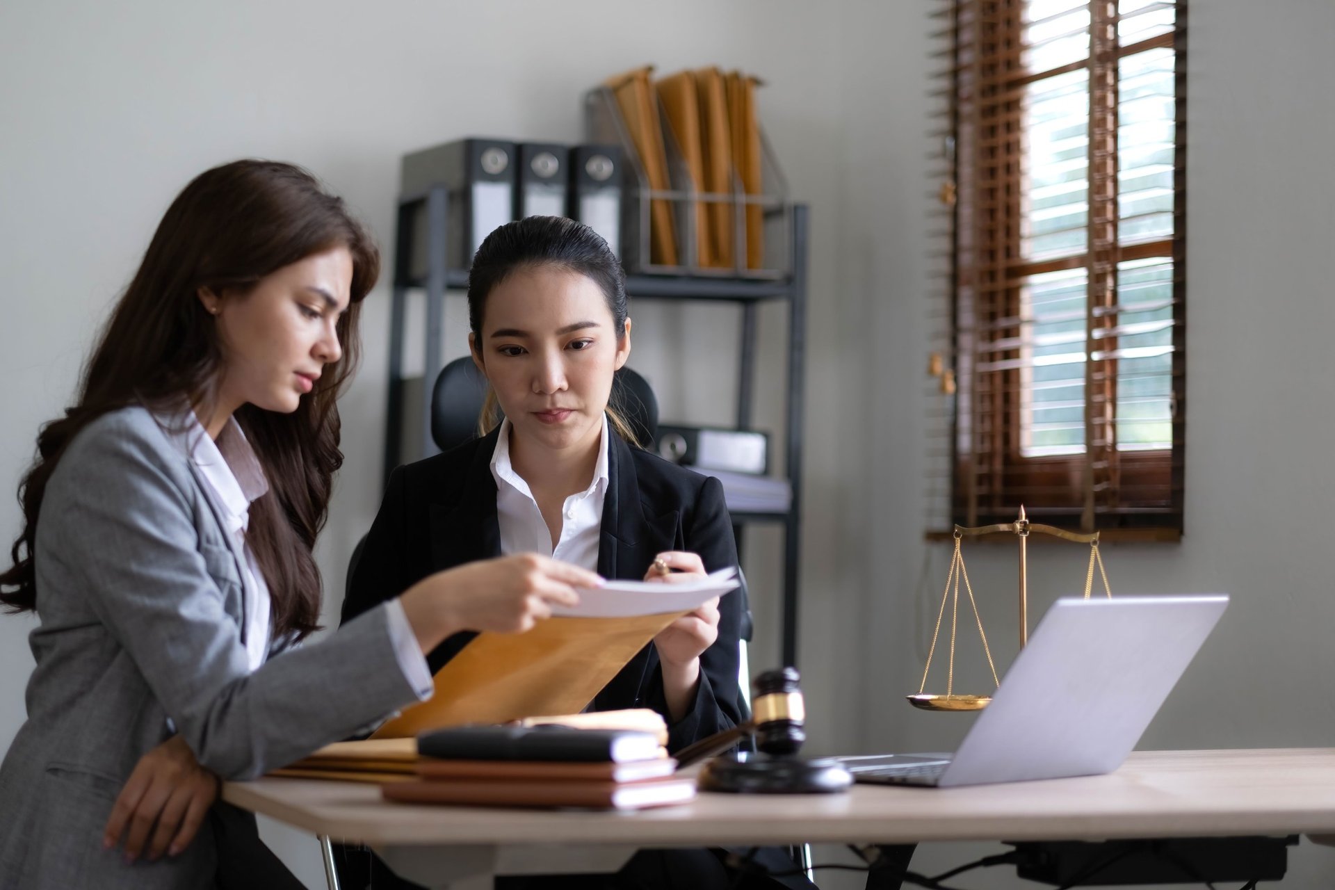 Female lawyers discussing legal papers in an office with justice scales and a laptop