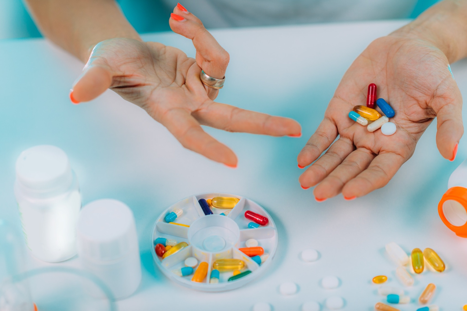 Hands displaying colorful pills and daily pill organizer on table