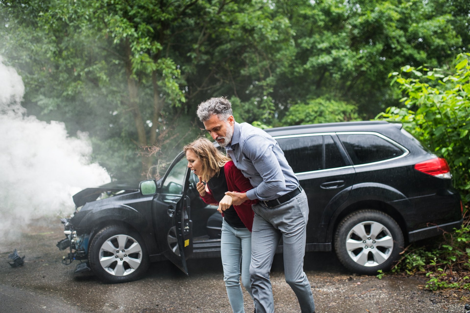 Man helping injured woman walk away from a smoking car after an accident