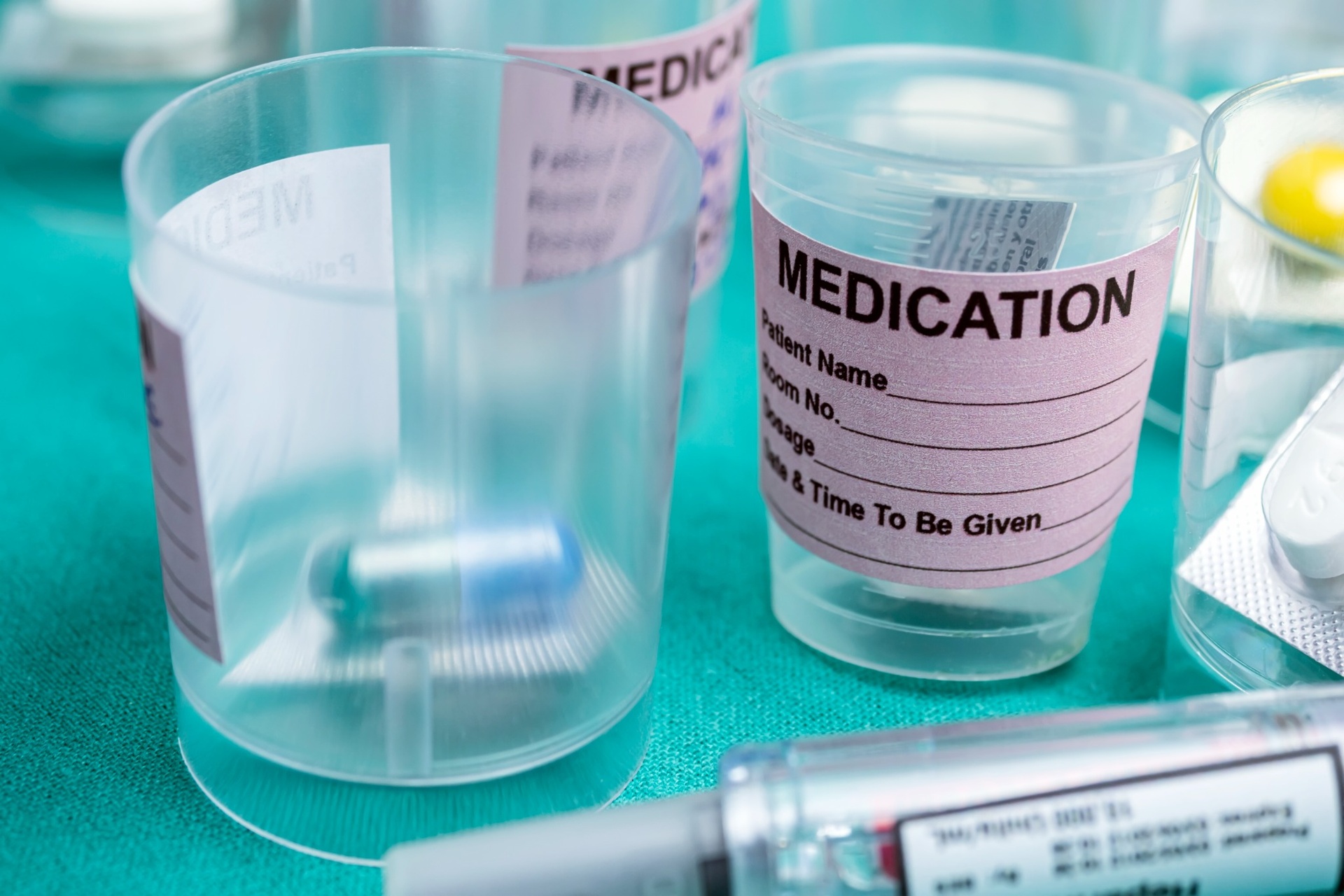 Medication cups labeled with dosage instructions on teal surface