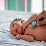 Newborn baby lying on bed during chest exam with stethoscope