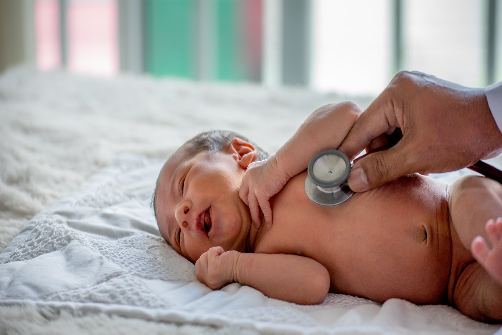 Newborn baby lying on bed during chest exam with stethoscope