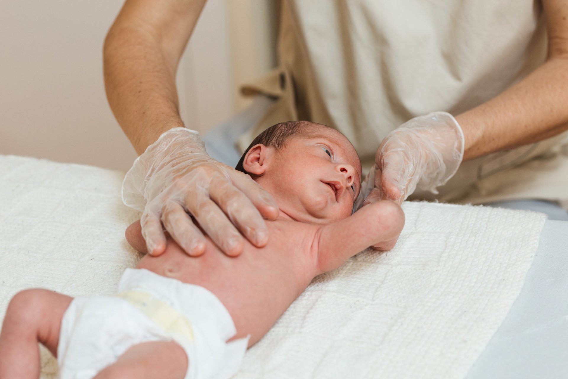 Physiotherapist evaluating newborn baby on white towel with gloves on