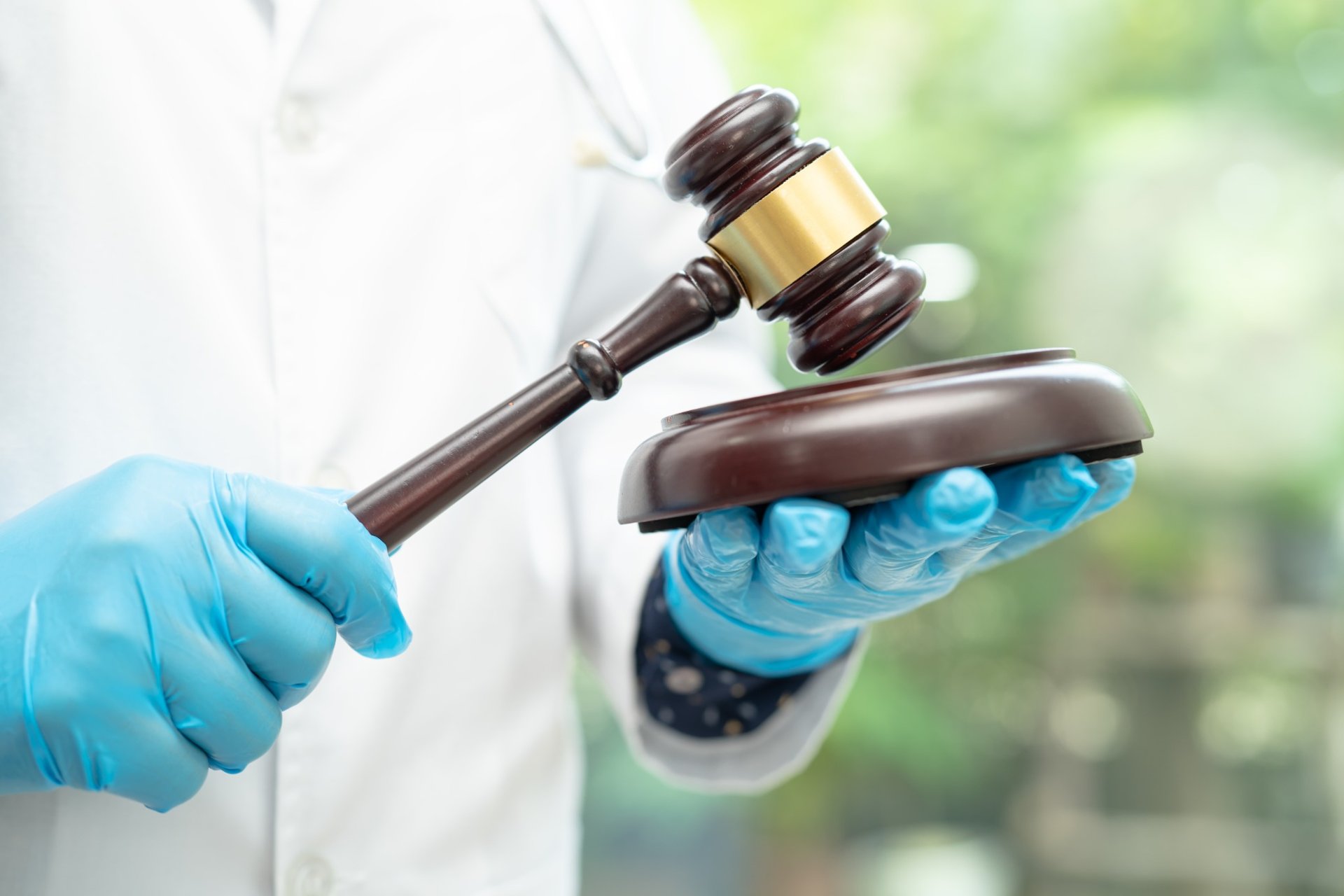 Doctor holding a judge's gavel wearing blue gloves, symbolizing medical-legal matters